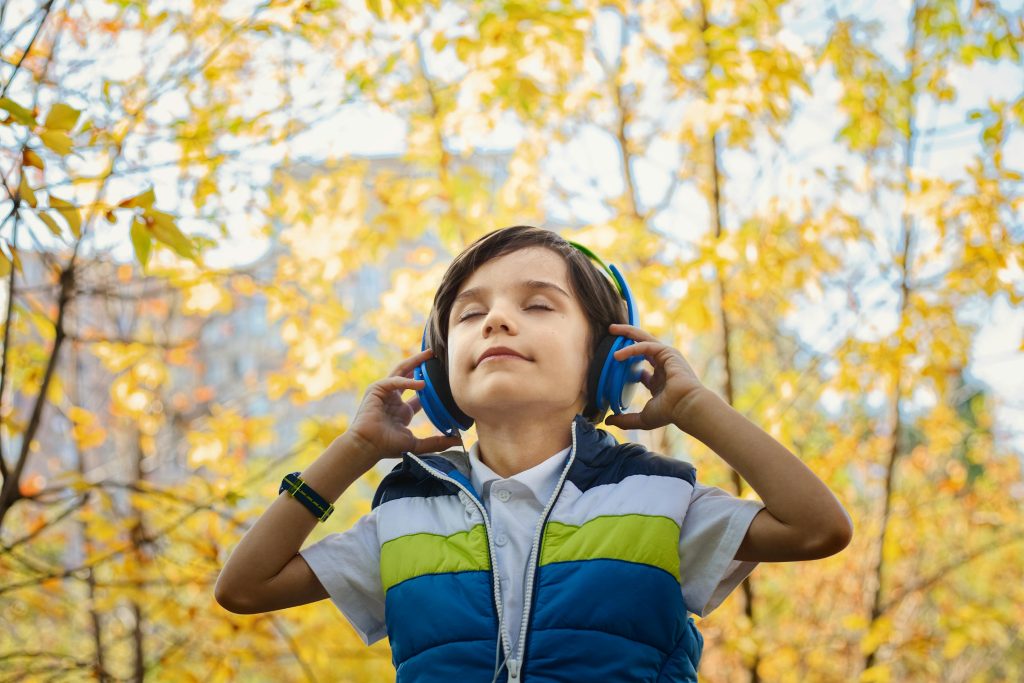 A young boy enjoys music through headphones amidst colorful fall foliage.