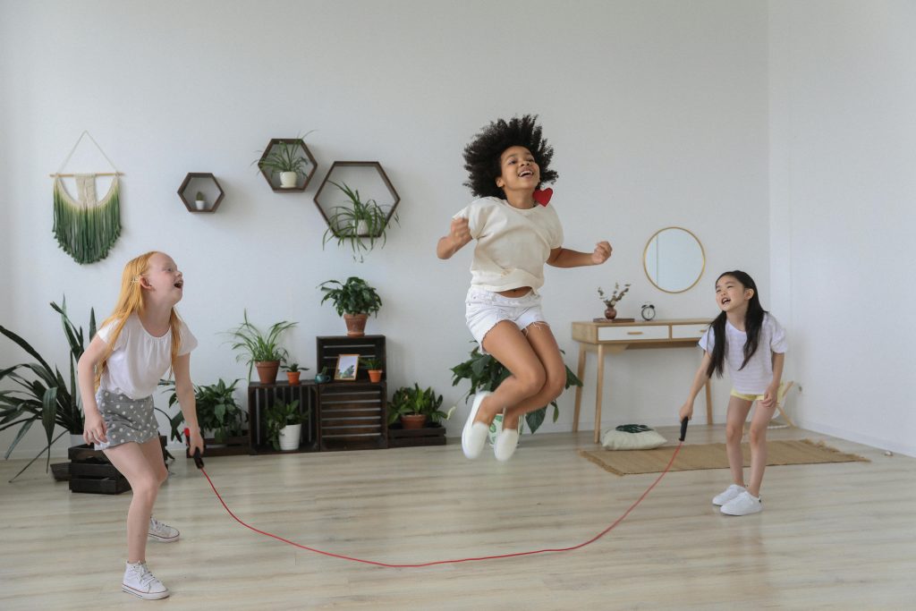 Three children laughing and jumping rope indoors, enjoying a fun and energetic playtime together.