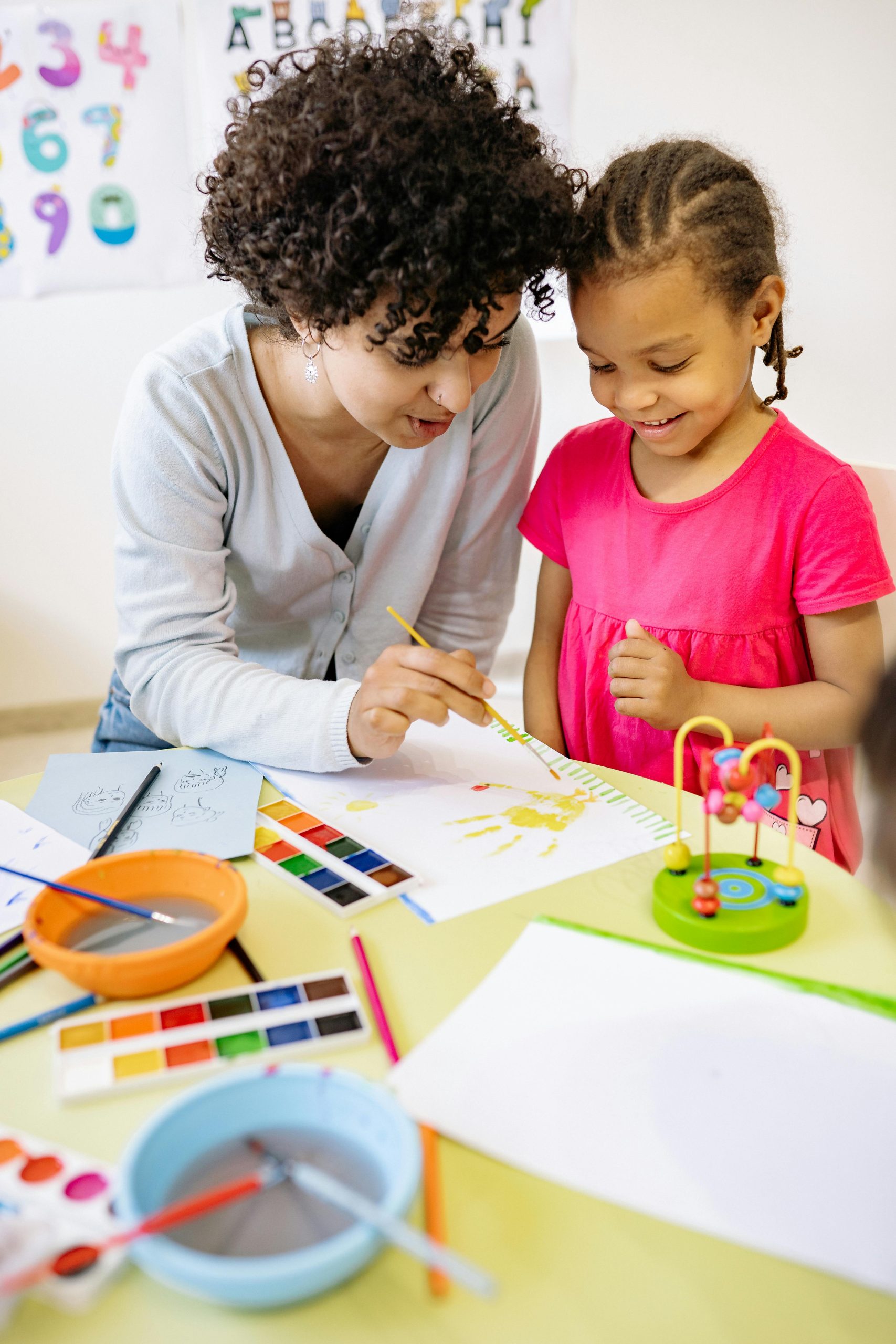 A teacher assists a child with painting, promoting creativity in an educational setting.