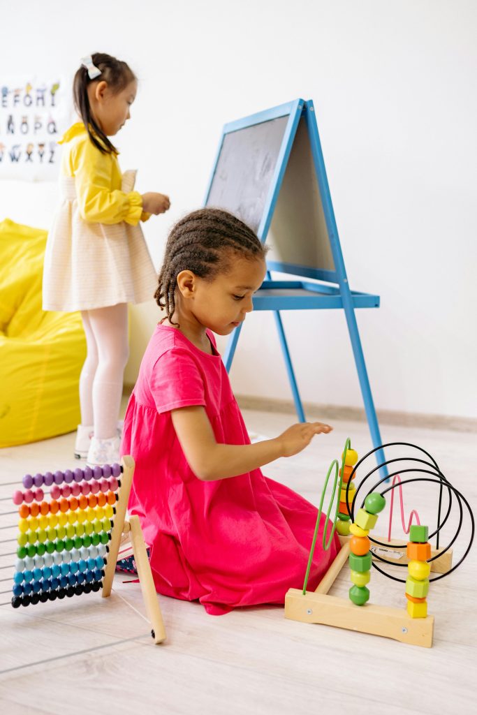 Two girls engaging in playful learning with abacus and toys in a bright classroom.